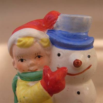 Fajance figur med glad dreng tæt op af glad snemand. Drengen har rød nisse hue på, grønt halstørklæde og gul bluse på.