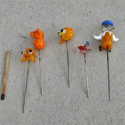5 stk. glasnipsenåle. Glashovederne forestiller bl.a. en orange elefant og en mand med blå hat.